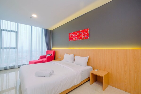 Quarto de hotel moderno com uma cama grande, uma cadeira vermelha, uma mesa de cabeceira de madeira e uma obra de arte vermelha na parede.