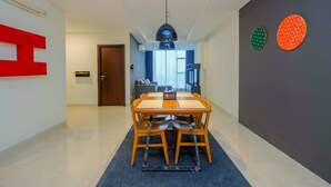 A modern dining area with a wooden table and chairs, a black ceiling lamp, and a large red letter 'E' on the wall. - Modern and Spacious 2BR L'Avenue Apartment (Jakarta)
