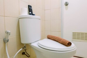 A toilet with a white tank, a towel on the seat, and a hand dryer on the wall. - Homey and Stylist 1BR Gading Icon Apartment (Jakarta)