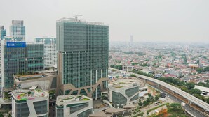Un moderno edificio de gran altura con fachada de vidrio, rodeado de otros edificios altos y una autopista.