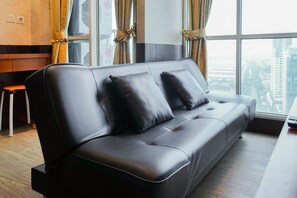 Un salon moderne avec un canapé en cuir noir, un plancher en bois et une grande fenêtre agrémentée de rideaux.