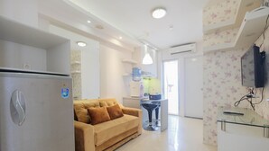 A modern kitchen with a refrigerator, a sofa, and a TV mounted on the wall.
