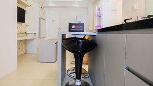 A modern kitchen with a black bar stool, a refrigerator, a water dispenser, and a flat-screen TV mounted on the wall.
