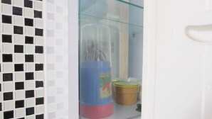 A bathroom with a glass partition, a blue container with a tiger design, and a brown container. - 2BR Homey Apartment at Bassura City near Mall (Jakarta)