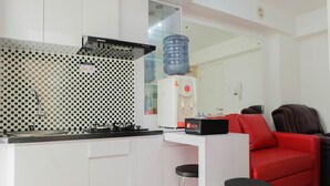 A compact kitchen with a checkered backsplash, a water dispenser, and a red sofa in the living area. - 2BR Homey Apartment at Bassura City near Mall (Jakarta)