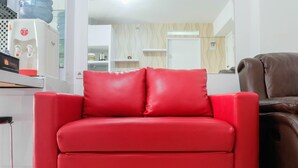 A red sofa in a modern living room with a water dispenser and a brown leather chair. - 2BR Homey Apartment at Bassura City near Mall (Jakarta)