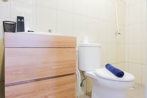 A bathroom with a wooden vanity, a white toilet, and a shower area. - Best Deal 3BR Bassura Apartment (Jakarta)