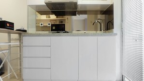 A modern kitchen with white cabinets, a stainless steel range hood, and a built-in microwave. - Stylish and Modern 2BR Bassura City Apartment (Jakarta)