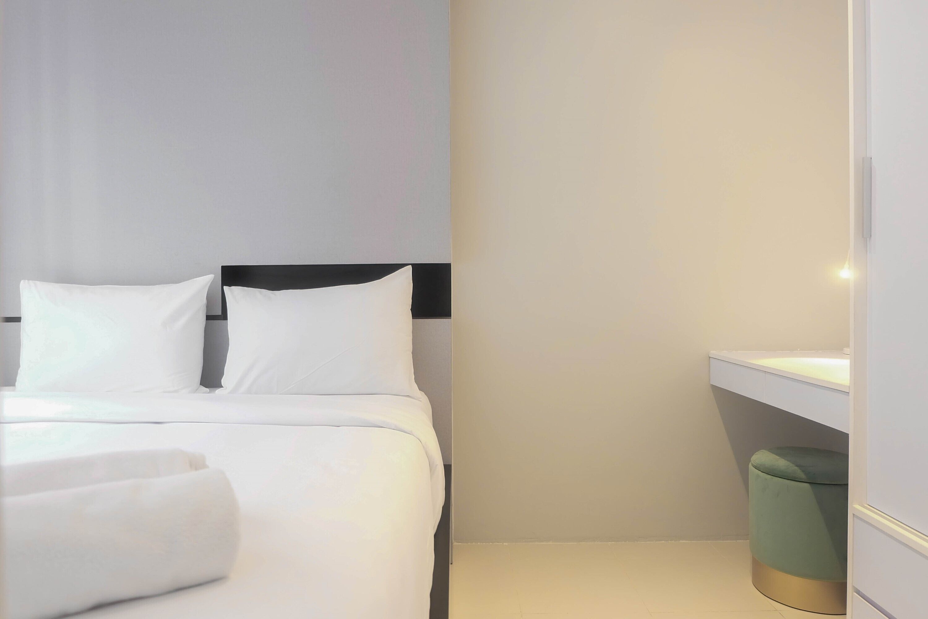 Habitación de hotel con una cama, una mesita de noche, un cubo de basura y una lámpara fijada a la pared.