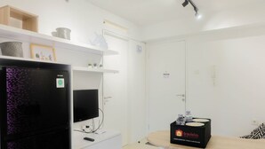 A modern hotel room with a flat-screen TV, a refrigerator, a dining table with a tray of complimentary food and beverage, and a white cabinet. - Stylish and Modern 2BR Bassura City Apartment (Jakarta)