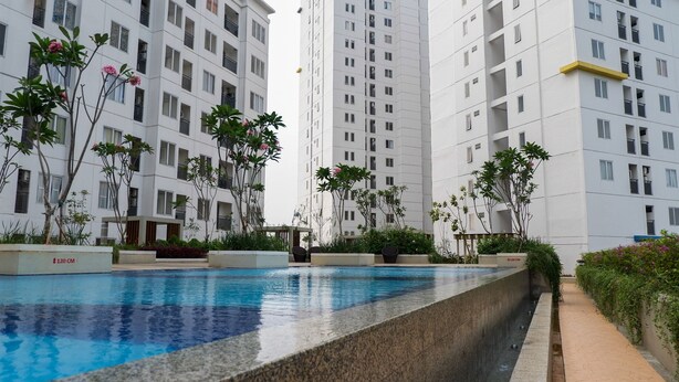 A swimming pool with a stone edge, surrounded by greenery and tall residential buildings. - Stylish and Modern 2BR Bassura City Apartment (Jakarta)