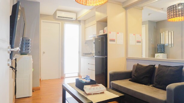A modern living room with a grey sofa, a small table with a cake, a TV, and a refrigerator. - Exclusive and Spacious 1BR Apartment at Bassura City (Jakarta)