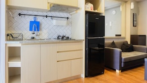 A compact kitchen with a black refrigerator, a built-in oven, and a microwave. There is a grey sofa in the adjacent living area. - Exclusive and Spacious 1BR Apartment at Bassura City (Jakarta)