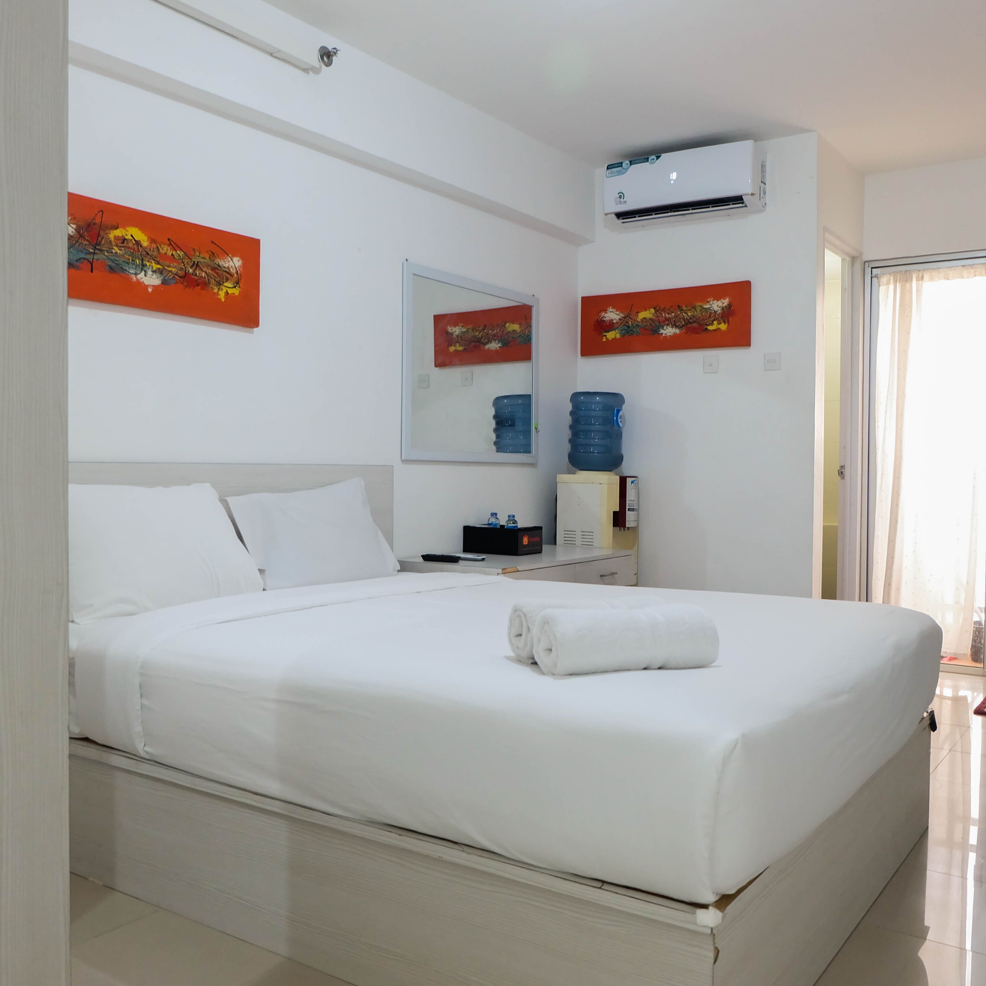 A neatly made bed in a hotel room with a large window, a water dispenser, and a wall-mounted air conditioner.