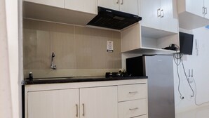 A modern kitchen with light-colored cabinets, a stainless steel refrigerator, and a black range hood. - Tidy Studio Apartment at Bassura City near Shopping Mall (Jakarta)
