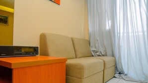 A room with a beige sofa, a wooden desk with a Grundig stereo system, and a white curtain.