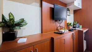 A reception desk with a flat-screen TV mounted above it, a potted plant, and a small table with a remote control and a calendar. - Comfy Studio Room Apartment at Kebagusan City (Jakarta)