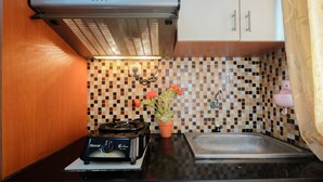 A kitchen with a black countertop, a Rinnai gas stove, a tiled backsplash, a stainless steel sink, and a potted plant. - Comfy Studio Room Apartment at Kebagusan City (Jakarta)