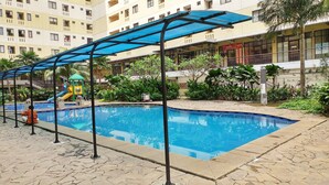 A swimming pool with a children's play area, surrounded by greenery and a multi-story building in the background. - Comfy Studio Room Apartment at Kebagusan City (Jakarta)