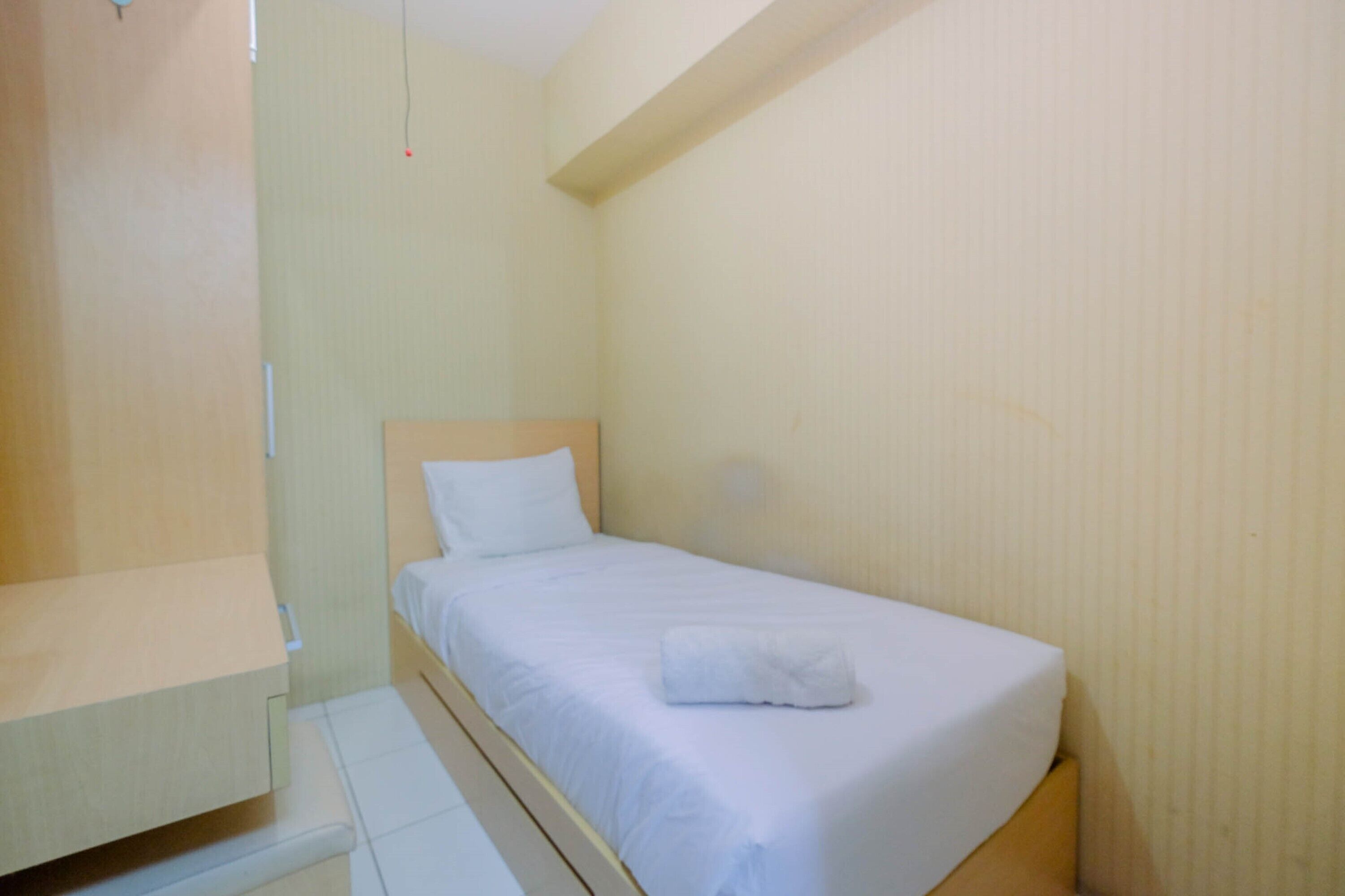 A small, single-bed room with a wooden headboard, a white bedspread, and a white pillow.