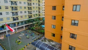 A multi-story residential building with balconies, a playground with play equipment, and a flagpole. - Warm and Homey 2BR Apartment at Kebagusan City (Jakarta)
