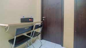 A small room with a dark wooden door, a beige wall, and a small table with two black chairs. There is a water bottle and a box on the table. - Warm and Homey 2BR Apartment at Kebagusan City (Jakarta)