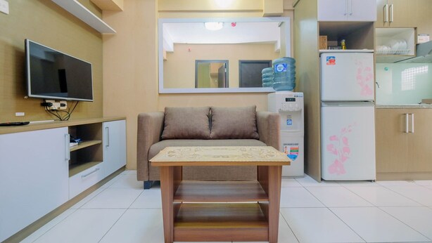 A compact living space with a sofa, a small table, a TV, a refrigerator, and a water dispenser. - Warm and Homey 2BR Apartment at Kebagusan City (Jakarta)