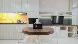 A modern kitchen with white cabinetry, a wooden dining table, and two white chairs. A travello branded bag is placed on the table. - Elegant and Comfy Studio Azalea Suites Apartment Cikarang (Cikarang)