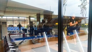 A gym with exercise equipment, a treadmill, and a mirrored wall reflecting a person running. - Elegant and Comfy Studio Azalea Suites Apartment Cikarang (Cikarang)