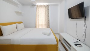 Een slaapkamer met een bed, een televisie, een nachtkastje en een raam met gordijnen.