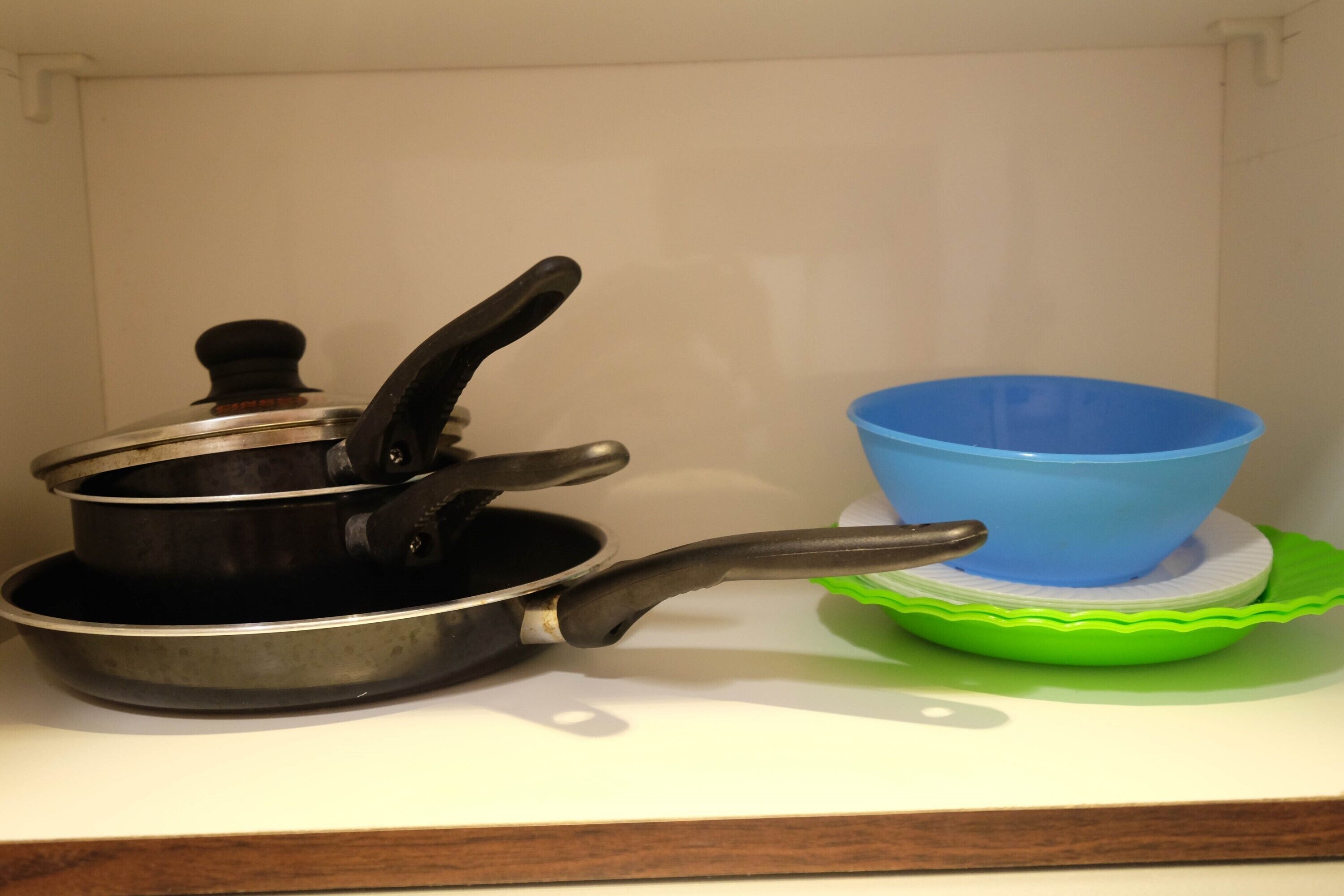 A kitchen counter with a frying pan, a blue bowl, and a green bowl on a white surface.