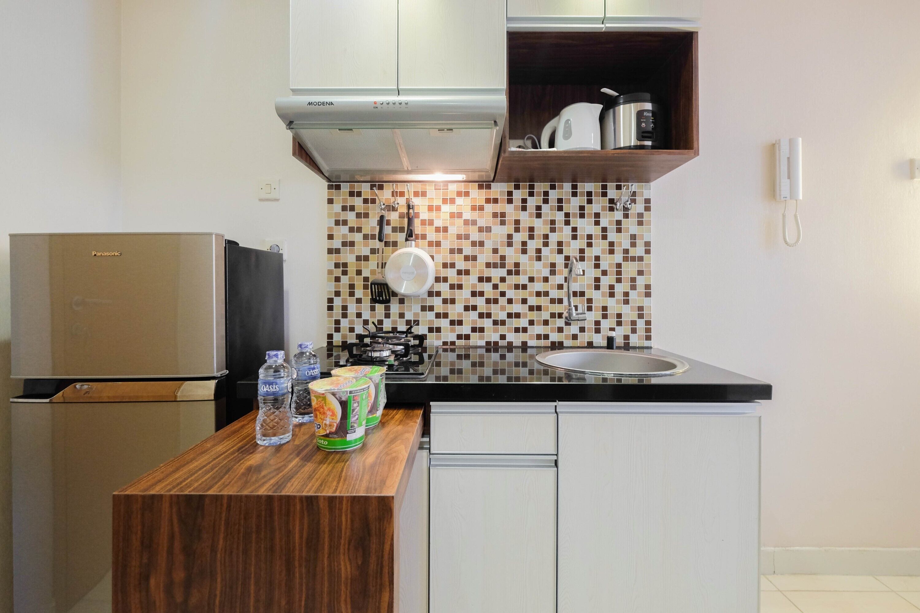 Una cucina compatta con frigorifero, fornello e un piano di lavoro in legno con bottiglie d'acqua e conserve.