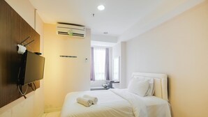 A hotel room with a bed, a television mounted on the wall, an air conditioning unit, and a window with curtains.