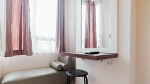 A small, modern room with a sofa, a stool, a wooden shelf with a remote control, and a mirror.
