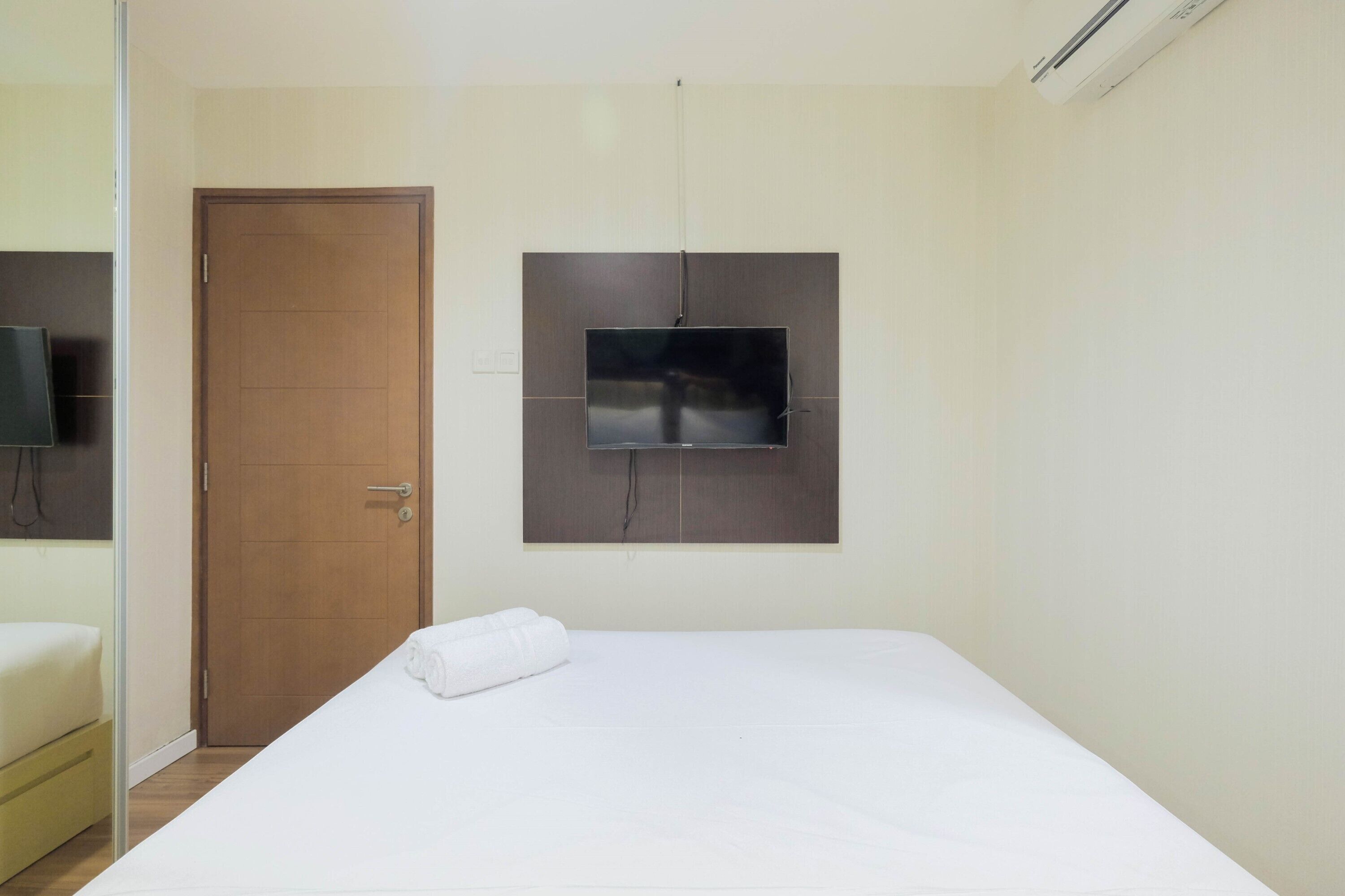 A hotel room with a bed, a television mounted on the wall, and a door.