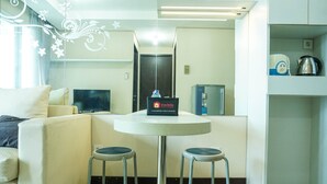 A modern hotel room with a sofa, a small round table with two stools, a flat-screen TV, a minibar, and a decorative wall with floral patterns. - 2Bedroom Sky Terrace Apartment with Pool View (Jakarta)
