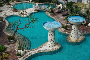 A large, uniquely shaped pool with a bridge, surrounded by tropical plants and decorative pillars. - 2Bedroom Sky Terrace Apartment with Pool View (Jakarta)