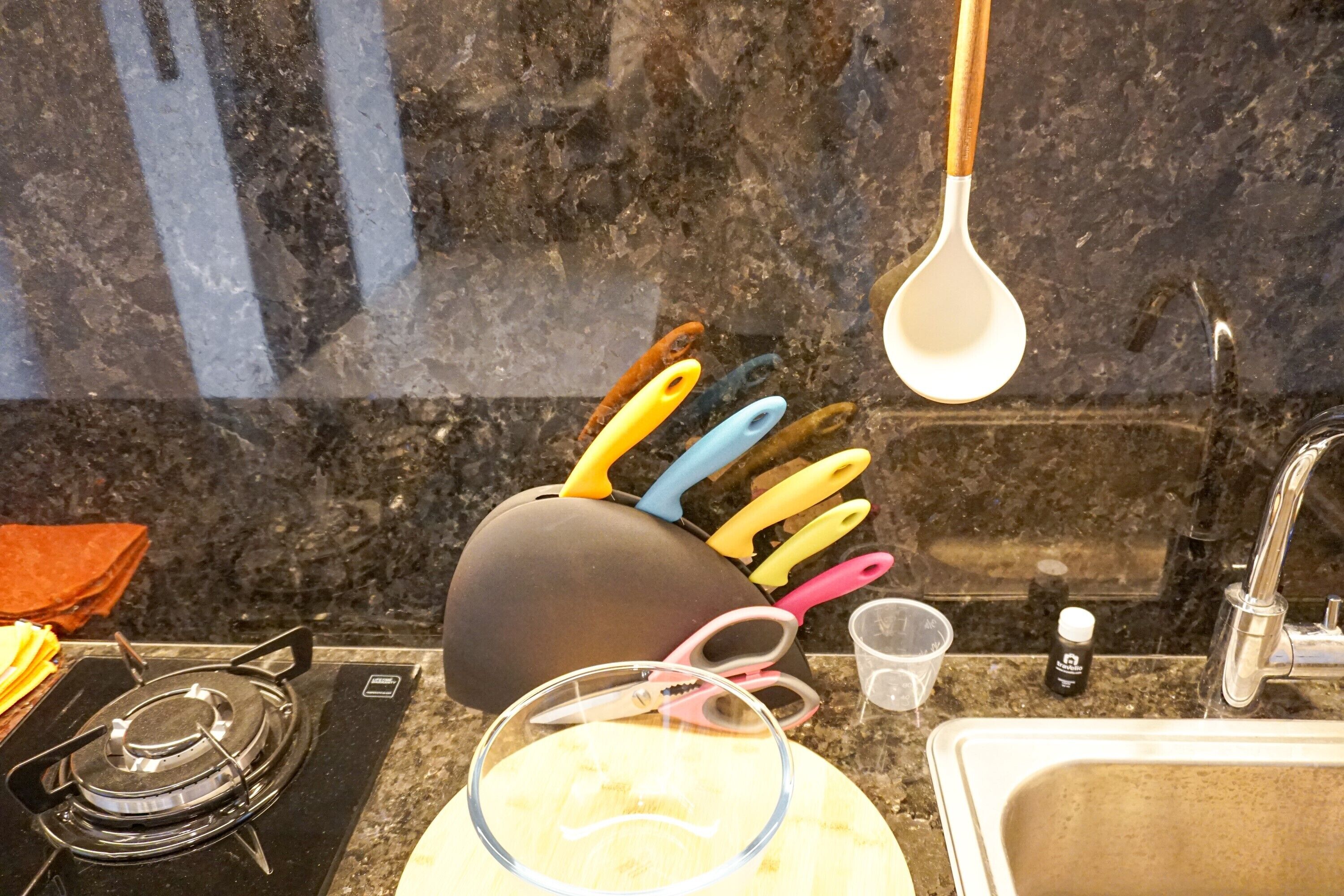 Une cuisine équipée d’une cuisinière à gaz, d’un évier et de divers ustensiles, notamment un manique et une louche.