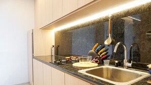 A modern kitchen with a granite countertop, stainless steel sink, and wooden cabinets. - Minimalist and Cozy 2BR Citralake Suites Apartment (Jakarta)