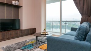 A modern living room with a flat-screen TV, a sofa, a coffee table, and a large window with a view of a cityscape. - Cozy and Comfy 2BR Citralake Suites Apartment (Jakarta)