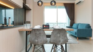 A modern kitchen with a dining area, two grey chairs, a blue sofa, and a city view. - Cozy and Comfy 2BR Citralake Suites Apartment (Jakarta)