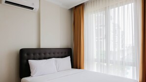 Habitación de hotel con cama, ropa blanca, cabecera negra, ventana con cortinas traslúcidas y unidad de aire acondicionado en la pared.