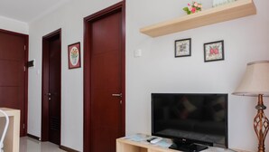 Habitación de hotel con un mueble bajo de madera para televisión, un televisor de pantalla plana, un estante de madera con objetos decorativos y dos cuadros en la pared.