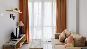 Una sala de estar con sofá, una mesa de centro, un televisor sobre un mueble bajo y una ventana con cortinas.