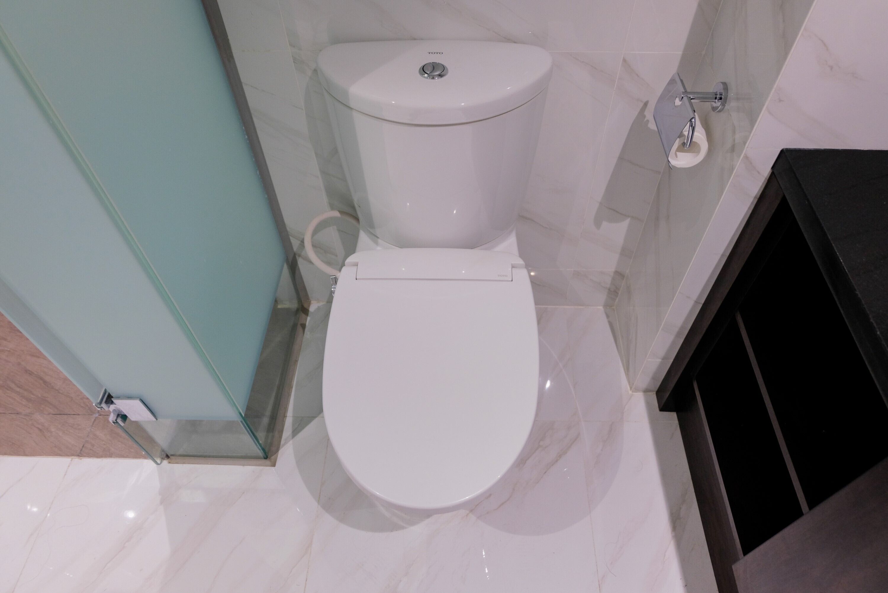 A modern bathroom with a white toilet, marble flooring, and a black cabinet.