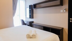 A hotel room with a bed, a desk, a clock, and a telephone on the wall.