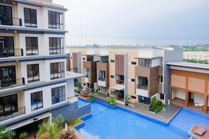 A modern multi-story residential building with a rooftop pool, balconies, and a view of the cityscape.