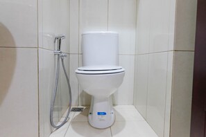 A white toilet with a bidet attachment in a tiled bathroom.