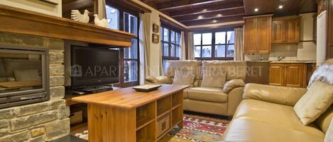 Ein gemütliches Wohnzimmer mit Kamin, Fernseher, Couchtisch aus Holz und beiger Couch.