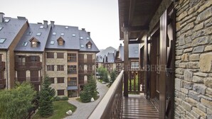 A balcony with stone walls and wooden railings overlooking a courtyard with buildings and trees. - Abetos - Val de Ruda (Baqueira)